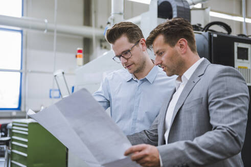 Zwei Geschäftsleute besprechen einen Plan in einer Fabrik - DIGF11132