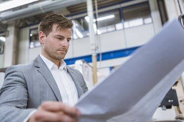 Businessman looking at plan in a factory - DIGF11134