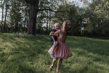 Happy girl carrying her little sister on a meadow - OGF00423