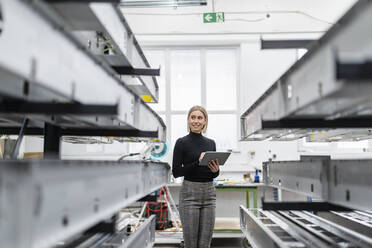 Frau hält Tablet an Metallstangen in Fabrikhalle - DIGF11155