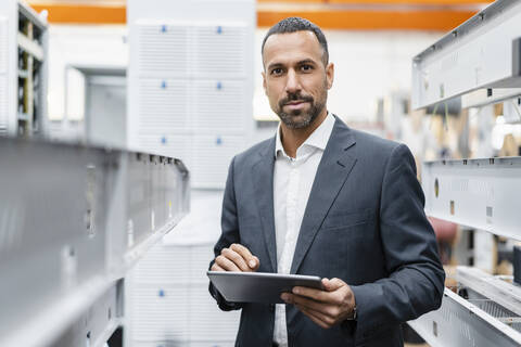 Porträt eines selbstbewussten Geschäftsmannes, der ein Tablet an Metallstangen in einer Fabrikhalle hält, lizenzfreies Stockfoto