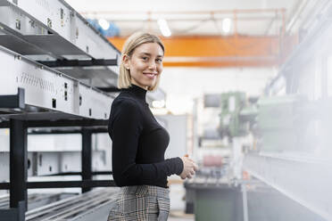 Porträt einer lächelnden Frau an Metallstäben in einer Fabrikhalle - DIGF11158