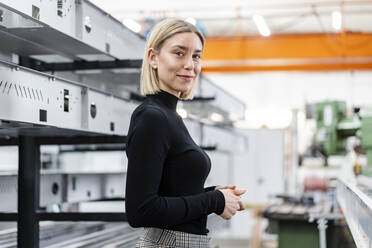 Porträt einer lächelnden Frau an Metallstäben in einer Fabrikhalle - DIGF11159