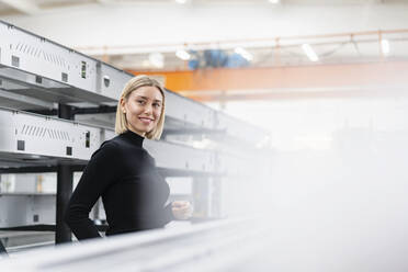 Porträt einer lächelnden Frau an Metallstäben in einer Fabrikhalle - DIGF11160