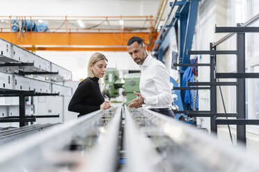 Geschäftsmann und Frau prüfen Metallstangen in einer Fabrikhalle - DIGF11161