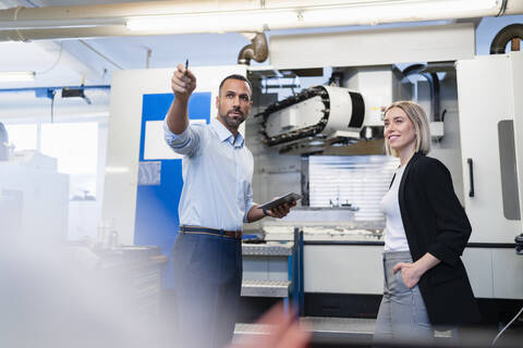 Businessman with tablet and woman having a meeting at a machine in factory hall stock photo