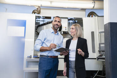 Geschäftsmann mit Tablet und Frau bei einer Besprechung an einer Maschine in einer Fabrikhalle - DIGF11215