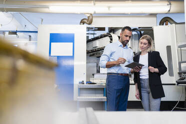 Businessman with tablet and woman having a meeting at a machine in factory hall - DIGF11216