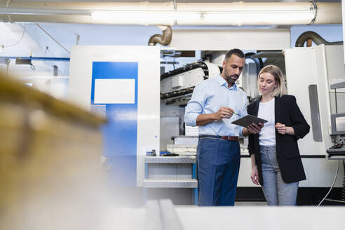 Geschäftsmann mit Tablet und Frau bei einer Besprechung an einer Maschine in einer Fabrikhalle - DIGF11216