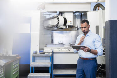 Geschäftsmann mit Tablet an einer Maschine in einer Fabrikhalle - DIGF11217