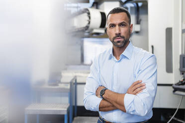 Portrait of confident businessman at a machine in factory hall - DIGF11220