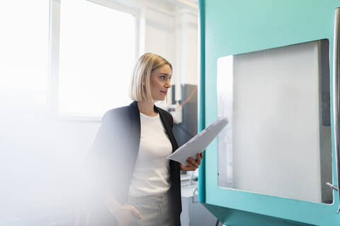 Woman with paper at a machine in factory hall stock photo