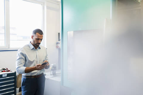 Geschäftsmann benutzt Mobiltelefon in einer Fabrikhalle, lizenzfreies Stockfoto