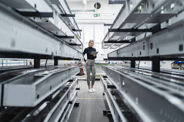 Frau mit Tablet an Metallstäben in Fabrikhalle - DIGF11232