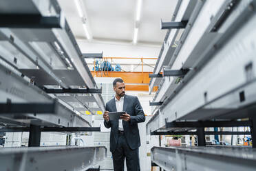 Businessman with tablet at metal rods in factory hall - DIGF11234