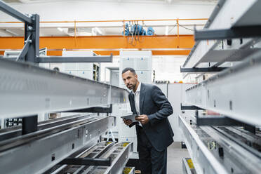 Businessman with tablet at metal rods in factory hall - DIGF11235