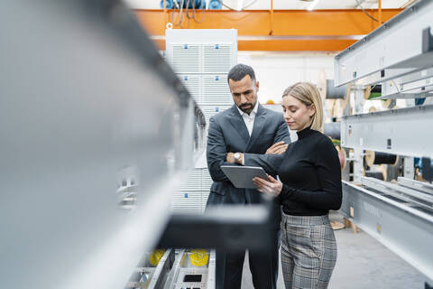 Businessman and woman with tablet at metal rods in factory hall stock photo