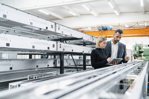 Geschäftsmann und Frau mit Tablet an Metallstäben in einer Fabrikhalle - DIGF11241