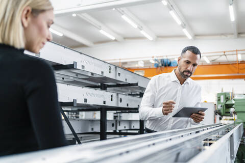 Businessman with tablet and woman at metal rods in factory hall stock photo