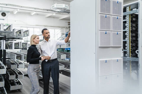 Geschäftsmann und Frau stehen an einer Maschine in einer Fabrikhalle, lizenzfreies Stockfoto