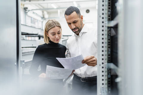 Businessman and woman with papers at a machine in factory hall stock photo