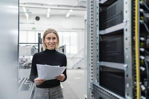 Smiling woman with papers at a machine in factory hall stock photo