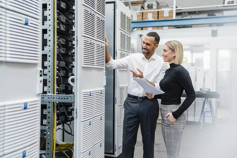 Smiling businessman and woman with papers at a machine in factory hall stock photo