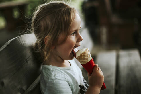 Mädchen isst Eiscreme auf einer Bank sitzend - VBF00090