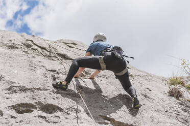 Young woman moving up while climbing rock against sky - FVSF00296