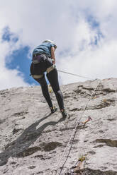 Junge Frau seilt sich beim Klettern gegen den Himmel an einem sonnigen Tag ab - FVSF00301