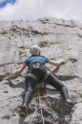 Junge Frau klettert mit Seil an einem sonnigen Tag auf einen Felsen - FVSF00305