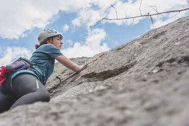 Junge Frau beim Klettern mit Blick auf Felsen gegen den Himmel - FVSF00306