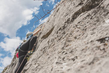 Woman moving up while climbing rock against sky on sunny day - FVSF00307