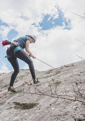 Young woman rappelling down with rope on rock against sky - FVSF00308