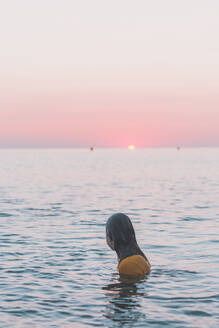Teenager-Mädchen badet bekleidet im Meer und beobachtet den Sonnenaufgang - FVSF00314