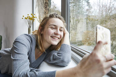 Portrait of happy young woman taking selfie with smartphone at home - FSF01079