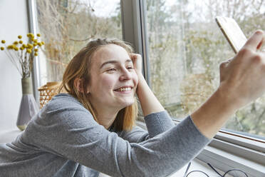 Porträt einer glücklichen jungen Frau, die zu Hause ein Selfie mit ihrem Smartphone macht - FSF01082