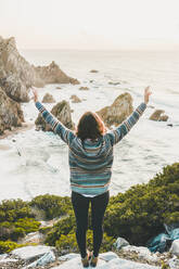 Young woman standing arms outstretched on rock at Ursa Beach, Lisboa Region, Portugal - FVSF00324