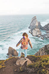 Junge Frau steht auf einem Felsen am Strand von Ursa, Region Lisboa, Portugal - FVSF00338