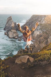 Junge Frau, die am Strand von Ursa auf einen Hügel springt, Region Lisboa, Portugal - FVSF00339