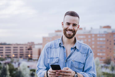 Portrait of relaxed young man with smartphone outdoors - EBBF00124