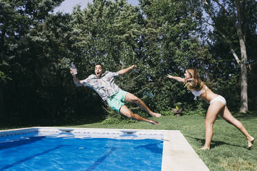 Verspielte junge Frau schiebt ihren Freund im Schwimmbad gegen Bäume - ABZF03141
