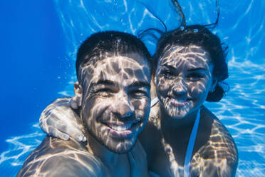 Lächelndes junges Paar schwimmt unter Wasser im Pool - ABZF03148