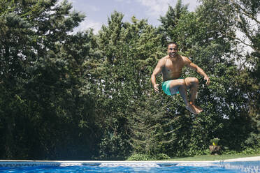 Cheerful handsome young man diving in swimming pool against trees - ABZF03149