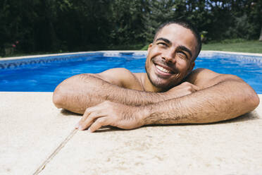 Lächelnder gutaussehender nasser junger Mann, der beim Entspannen im Schwimmbad wegschaut - ABZF03150