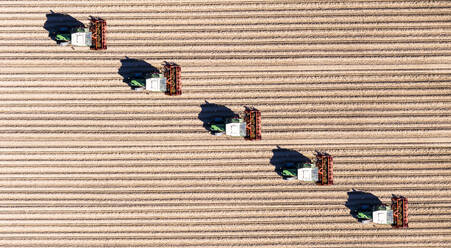 Germany, Hesse, Bergstarsse, Aerial view of tractors plowing brown field in spring - AMF08117