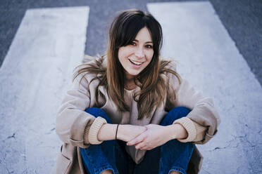 Porträt einer lächelnden jungen Frau, die auf einem Zebrastreifen sitzt - EBBF00157
