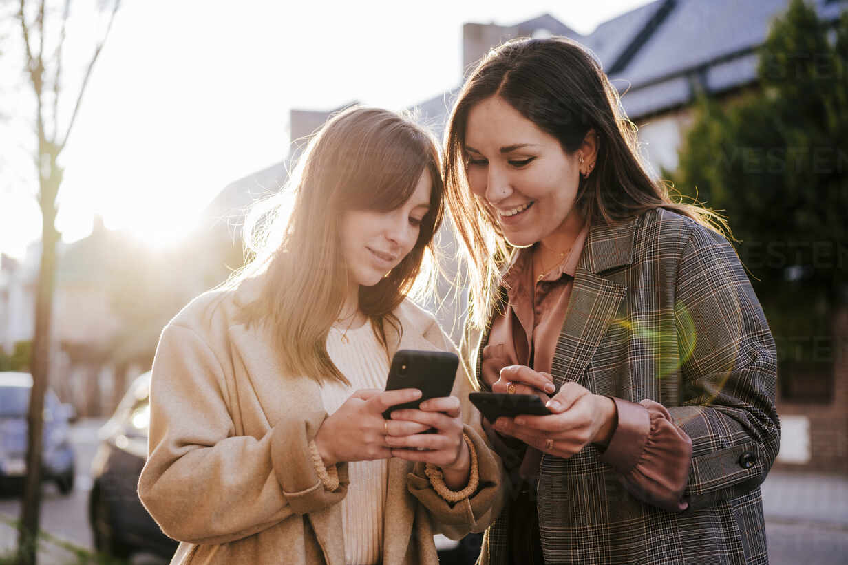 Portrait of two best friends looking at cell phone at backlight stock photo