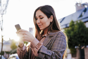 Portrait of woman looking at cell phone at backlight - EBBF00161