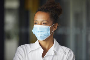 Portrait of businesswoman wearing light blue protective mask looking at distance - RBF07688